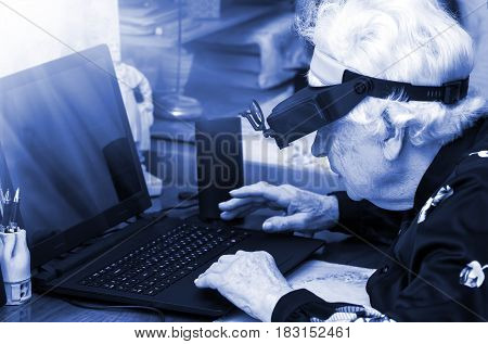 grandmother learns to work at home on the computer and internet In big special glasses virual reality, blue tone