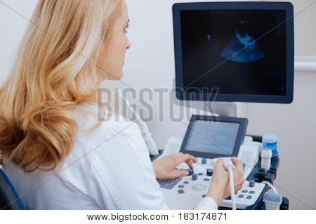 Expressing my full attention at work. Proficient beautiful involved sonographer working in the clinic and looking for digital image while providing ultrasonic examination