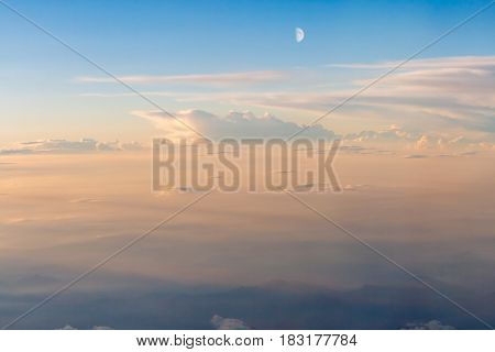 The colorful soft sky above the clouds with half moon and some mountains silhouettes below - airplane traveling in the summer