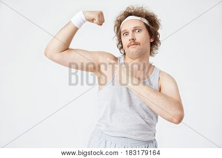 Closeup portrait of man in old-fashioned sportswear showing big guns, pointing with left hand