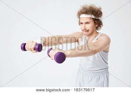 Weak retro man in old-fashioned sports wear training with hand weights. Looking exhausted