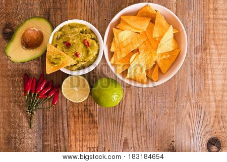 Guacamole dip and nacho chips on wooden table.