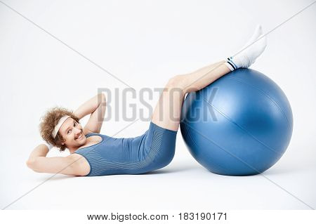 Doing abdominal crunches. Man curling up with legs on exercise ball. Smiling, looking glad
