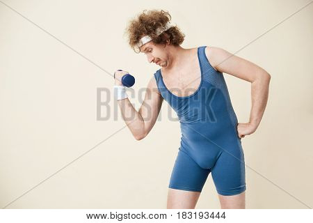 Out of date sport clothing. Man working on arm muscles, training with ligh dumbbell