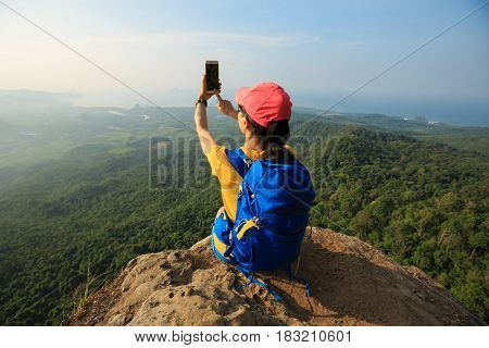 successful woman hiker taking photo with smartphone on mountain peak cliff