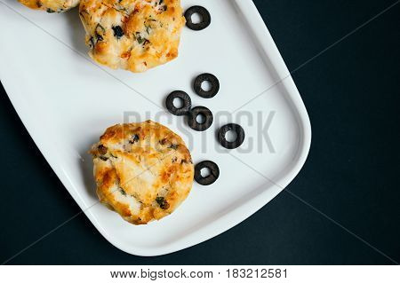 Cupcakes with spinach, cheese and vegetables on a black background. Healthy breakfast concept. Pieces of sliced olives.