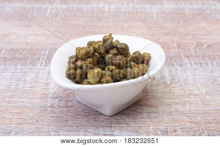 bowl with fresh capers on wooden table.