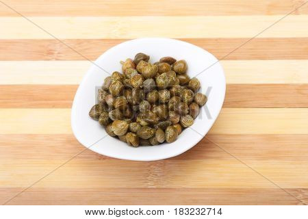 bowl with fresh capers on wooden table.