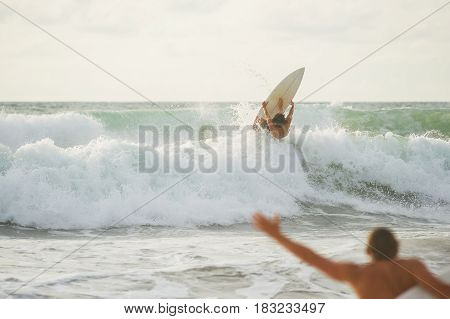 Surfer with a tanned body performs a trick on a short board - a jump over the waves. Extreme water sports, fun at the oceanfront surfing. The surfer rolls on the waves at sunset.