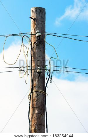 Old wooden pillar with power line against the blue sky. A botched electrical connections