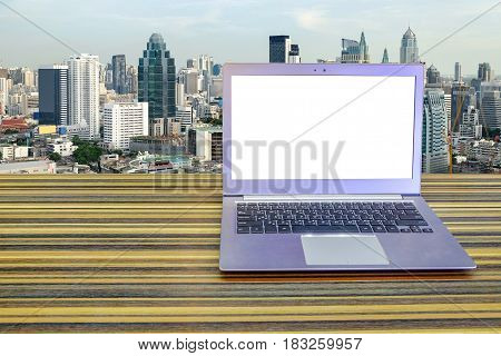 Laptop whit blank screen on long table with Cityscape background, Exterior office.