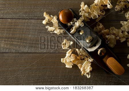 Woodworking hand planer tool on wooden boards in carpenter's workshop against dark brown background with copy space