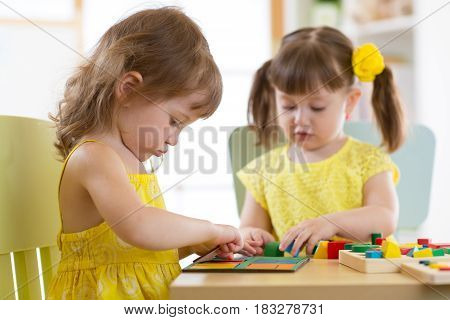 Kids girls playing with logical toy on desk in nursery room or kindergarten. Children arranging and sorting shapes, colors and sizes.