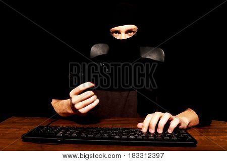 Dangerous hacker in balaclava holding gun