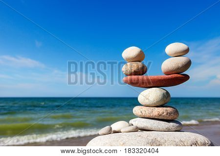 Stones balance on the background of sea and blue sky. Rock zen in the form of scales. The concept of balance