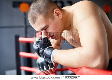 Side view portrait of sweaty exhausted shirtless boxer resting, catching breath after hard fight in boxing ring