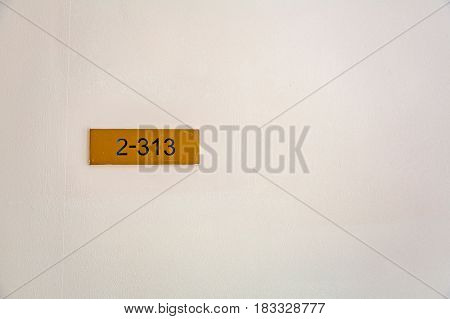 Yellow nameplate with black figures 2-313 hanging on a light wall