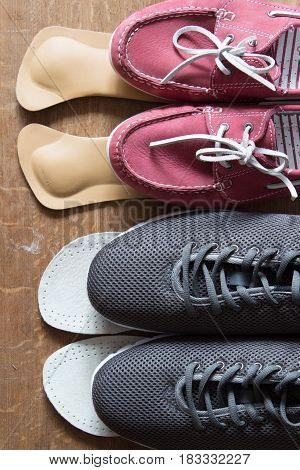 Gray sport shoes and pink sneakers with orthopedic insoles. Wooden background.