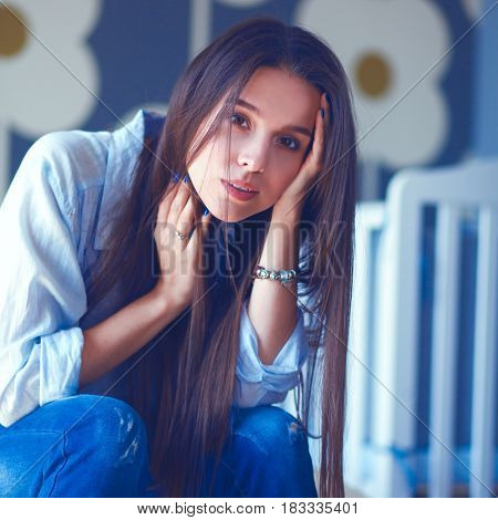 Young tired woman sitting on the bed near childrens cot.