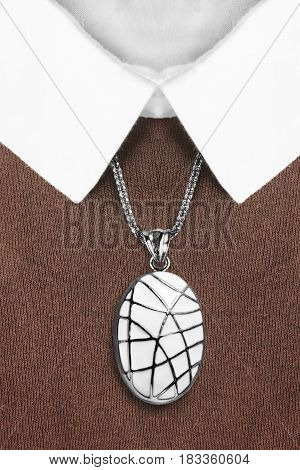 Elegant white enameled medallion over brown pullover with white collar closeup