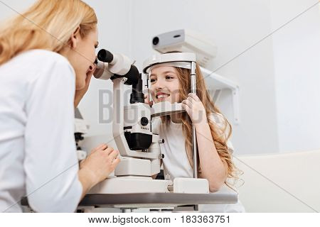 Do not move. Regular scrupulous distinguished specialist holding a consultation observing her patients eyes while employing ophthalmoscope