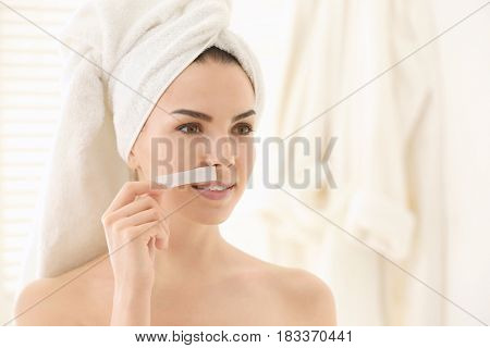 Young woman removing facial hair with wax on blurred background