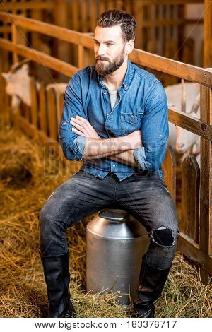 Portrait of a handsome farmer sitting on the retro milk container at the goat barn. Natural milk production and farming concept
