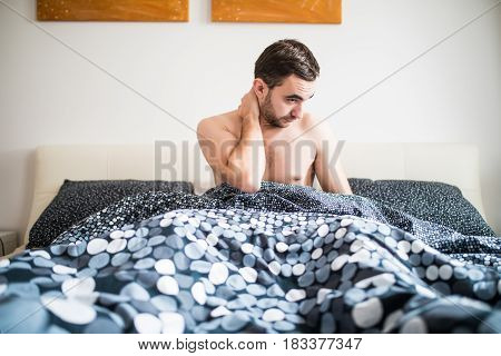Young Man Suffering From Neckache In Bedroom At Home