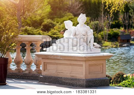 Marble statue of greek goddess with naked breast and cupid in the park
