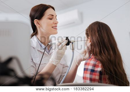 Everything is cool. Satisficed female medical worker keeping smile on her face looking attentively into ear of little girl while touching it