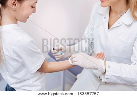   Smiling girl standing opposite her doctor giving hand for prick while bowing her head