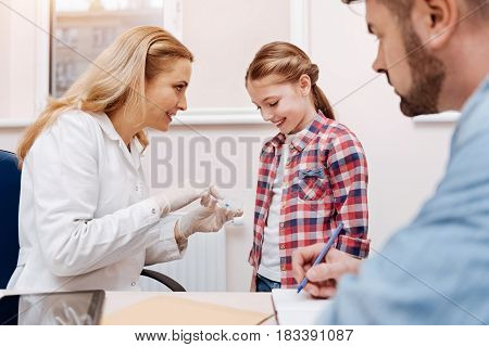  Confident family doctor sitting at her workplace wearing white smock showing box with pills to her visitor while giving some explanations