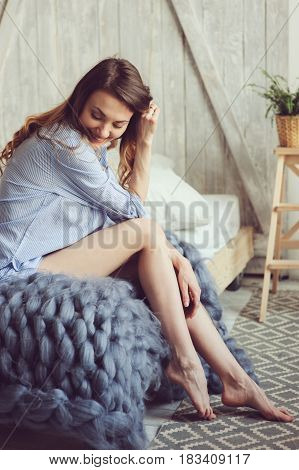 young woman in pajama wake up in the morning in cozy scandinavian bedroom and sitting on bed with houseplants on background. Casual lifestyle in modern interior