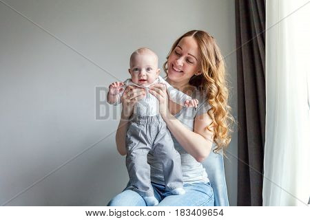 Young mother holding her newborn child. Woman and new born boy relax in a white bedroom with blue chair. Mother breast feeding baby. Family at home