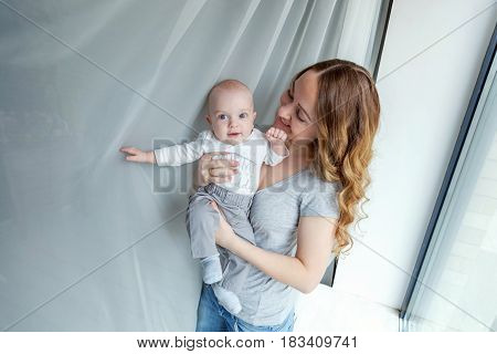 Young mother holding her newborn child. Woman and new born boy relax in a white bedroom near the windiow. Mother breast feeding baby. Family at home. Young mother playing whith her newborn son
