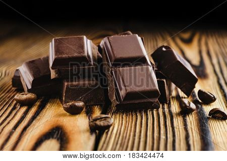 Pieces of bitter dark chocolate cubes on heap and coffee bean on wooden background close-up view.