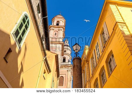Belfry of Saint-Michel Archange basilica among colorful houses under blu sky in old town of Menton, France.
