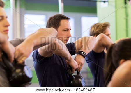 sport, fitness, weightlifting and people concept - man with kettlebell and heart-rate tracker at group training exercising in gym
