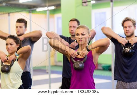 sport, fitness, weightlifting and training concept - group of people with kettlebells exercising in gym