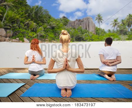 fitness, sport, yoga and healthy lifestyle concept - group of people exercising in reverse prayer pose over tropical beach background