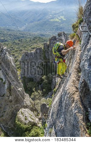 Male climber in special outfit climbing cliff with mountaineering equipment