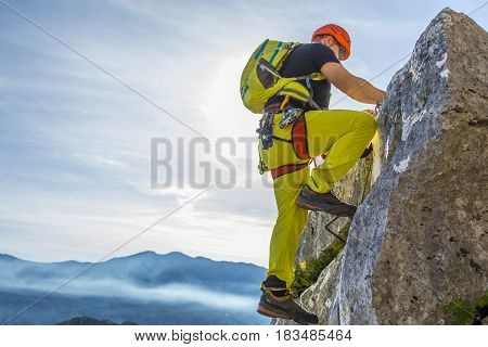 Male alpinist in special outfit climbing rock on background of summit and sky