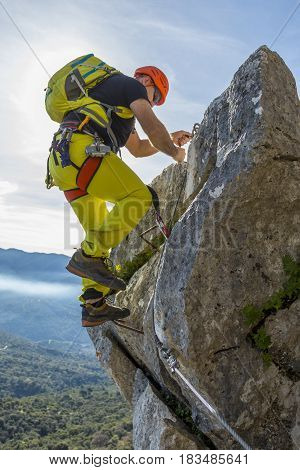 Male alpinist in special outfit climbing rock on background of summit and sky