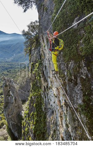 Side view of male climber clinging cliff with mountaineering equipment on background of landscape
