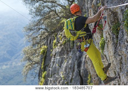 Male climber in special outfit climbing cliff with mountaineering equipment
