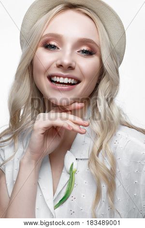 Young smiling girl with curls in a hat. A beautiful model in a white shirt and a brooch-flower. Gentle makeup. Summer light image. Beauty of the face.