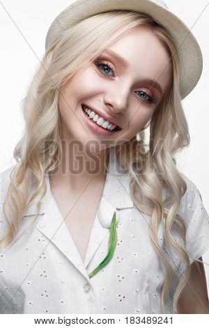 Young smiling girl with curls in a hat. A beautiful model in a white shirt and a brooch-flower. Gentle makeup. Summer light image. Beauty of the face.