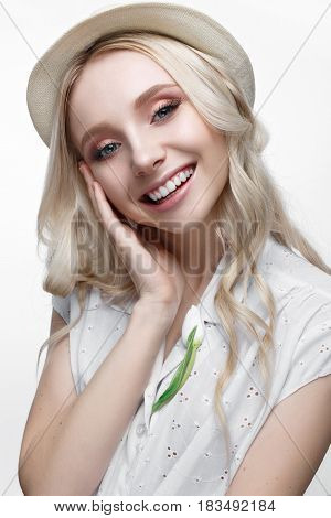 Young smiling girl with curls in a hat. A beautiful model in a white shirt and a brooch-flower. Gentle makeup. Summer light image. Beauty of the face.