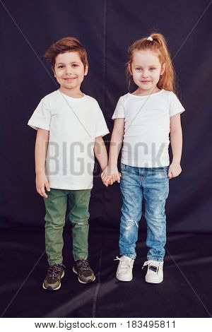 Two children in blank white t-shirts stand holding hands on black background.