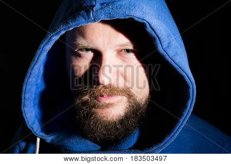 Solid bearded middle-aged man in a hood  portrait on black background